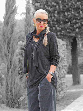 Eine reife Frau trägt das OFF#DLY Longsleeve Sigrid black mit feinem Rippenstrick und passendem Schal, kombiniert mit weiten Hosen und auffälligen Accessoires.