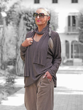 Person mit silbergrauem Zopf trägt das OFF#DLY Longsleeve Sigrid schoko, ein geripptes Langarmshirt mit passendem Schal, kombiniert mit weiten Cordhosen. Elegante Accessoires runden den Look ab.