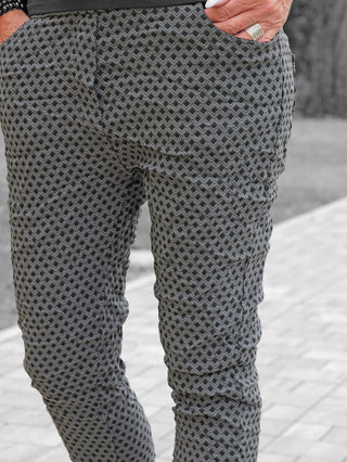 OFF#DLY Muster-Pant Saga grey/black zeigt schlanke, graue Hosen mit rautenförmigem Muster, getragen auf einem Gehweg. Hand mit silbernen Ringen in der Tasche, betont den stilvollen Look.