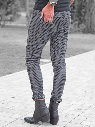 OFF#DLY Muster-Pant Saga grey/black: Schmale Hose mit geometrischem Print in Grau und Schwarz, kombiniert mit schwarzen Lederstiefeletten und Accessoires wie Ringen und einer Apple Watch mit Leopardenmuster-Armband.