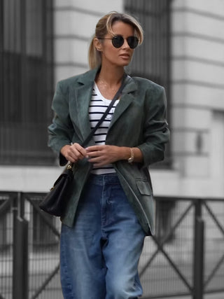 Frau trägt den Gitta Banko Blazer Amy khaki, gerade geschnitten, über einem gestreiften T-Shirt und Jeans, kombiniert mit runder Sonnenbrille und schwarzer Umhängetasche in urbaner Umgebung.