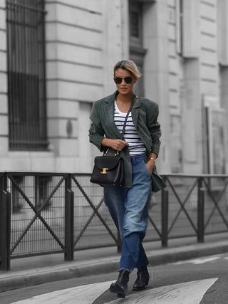 Frau im Gitta Banko Blazer Amy khaki, gerade geschnitten und oversized, kombiniert mit Streifen-Shirt und Jeans, lässig und modern auf einer Stadtstraße gehend.