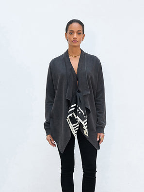 Model trägt einen Outryght Mara B faded black: ein dunkelgrauer Wasserfall-Cardigan über schwarzem Top, mit schwarz-weiß gemustertem Schärpe; kombiniert mit schmalen schwarzen Hosen und dezentem Schmuck.