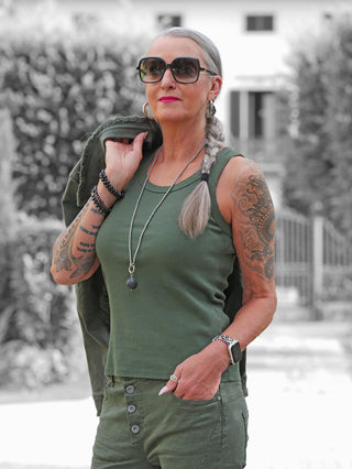 Eine selbstbewusste Frau trägt das olivefarbene OFF#DLY Top Neve. Das gerippte Baumwoll-Top passt perfekt zu ihrer eleganten Hose und ergänzt ihren modischen, sommerlichen Look.