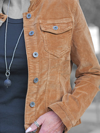 OFF#DLY Jacke Elettra Zimt: Tan-braune Cordjacke mit Metallschnappverschlüssen, getragen über einem schwarzen Oberteil, kombiniert mit einer silbernen Kette und silbernen Ringen an der linken Hand.