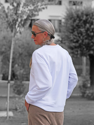 Person mit silbernem Zopf trägt ein OFF#DLY Sweat Latte Choco white. Weißes Sweatshirt, modern und lässig, kombiniert mit großen Ohrringen und Sonnenbrille im Park.