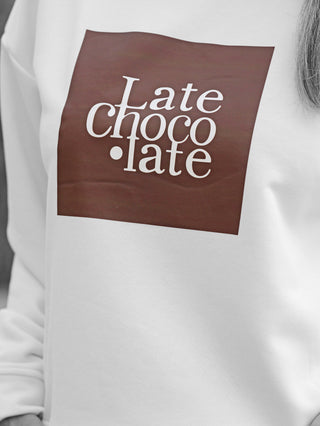 Nahaufnahme eines weißen OFF#DLY Sweat Latte Choco mit schokoladenbraunem Aufdruck Late Choco·late im Quadrat auf der Vorderseite, bequem geschnitten aus Baumwoll-Polyester-Mix, ideal für lässige Outfits.