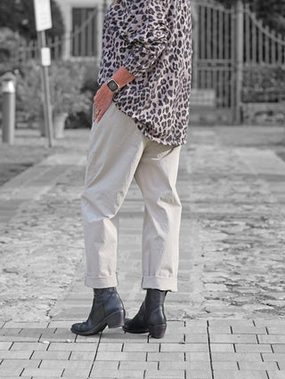 Die OFF#DLY Pant Melania stone in hellbeige, mit geradem Bein und hochgekrempelten Bündchen, kombiniert mit schwarzen Lederstiefeletten und einer Smartwatch, zeigt ihren lässigen, vielseitigen Stil.