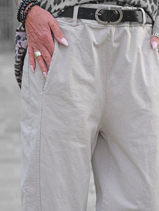 Nahaufnahme der OFF#DLY Pant Melania stone: Leichte beige Hose mit schwarzem Ledergürtel. Hand in der Seitentasche, modische Accessoires, darunter ein silberner Ring und dunkle Armbänder sichtbar.