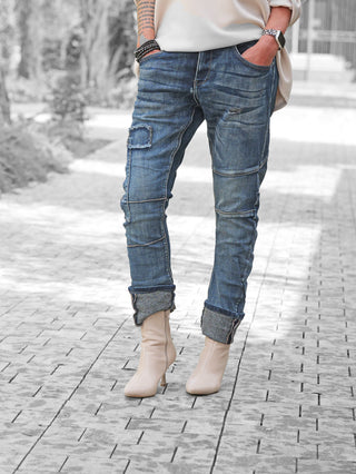 Person trägt OFF#DLY Denim Ilaria darkblue Jeans mit Destroy-Details und umgeschlagenen Säumen, kombiniert mit beigefarbenen Stiefeletten. Tätowierter Unterarm und Accessoires sichtbar.