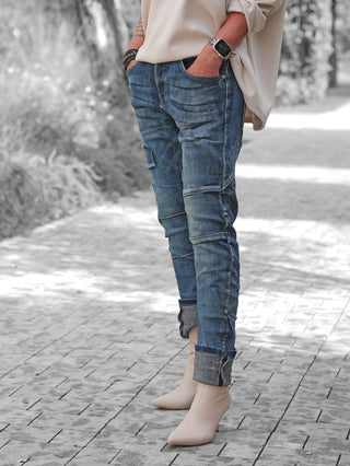 OFF#DLY Denim Ilaria darkblue: Slim-fit Jeans mit umgeschlagenen Bündchen und Destroy-Details, getragen mit beige Stiefeletten, präsentiert lässig und trendig auf einem gepflasterten Weg, betont durch Accessoires am Handgelenk.