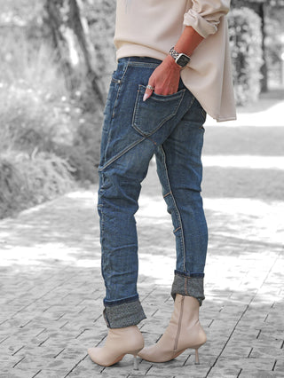 Nahaufnahme von OFF#DLY Denim Ilaria darkblue Jeans mit lässigem, leicht verwaschenem Design, markanten Nähten und Destroy-Details, getragen mit beigen Stiefeletten und einer Hand in der Gesäßtasche.