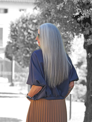 Person von hinten mit langem, silbernem Haar, trägt den OFF#DLY Sweater Varda in Dunkelblau, kombiniert mit einer braunen, plissierten Midirock. Der Sweater wirkt minimalistisch und edel.
