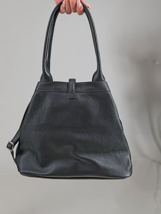 OFF#DLY Leder Tasche black: Schwarze Ledertasche im Tote-Stil mit leicht genarbter Oberfläche, zwei Schulterriemen, einstellbarem Seitenriemen mit Metallschnalle und einfachem Tabverschluss, von Hand mit neutralem Nagellack gehalten.