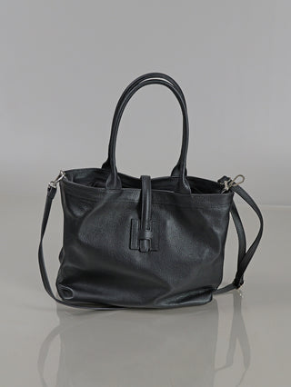 Die OFF#DLY Leder Tasche black ist eine mittelgroße, schwarze Ledertasche mit zwei runden Henkeln, abnehmbarem Schulterriemen, körniger Struktur und einem Tab-and-Loop-Verschluss vorne.