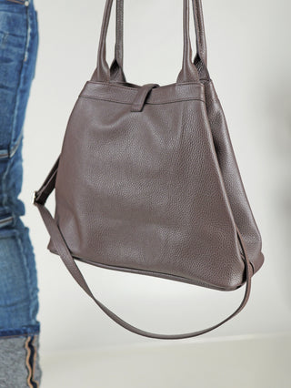 OFF#DLY Leder Tasche schoko: Mittlere, genarbte Ledertasche in Braun, mit zwei kurzen Griffen und einem längeren, verstellbaren Schulterriemen. Sichtbar ist ein Teil einer Person in blauen Jeans.