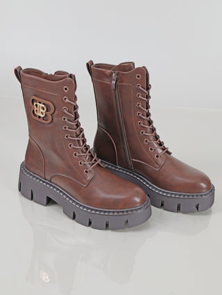 OFF#DLY Boot BB brown: Mittelhohe, braune Schnürstiefel mit seitlichem Reißverschluss, dicker Plateausohle, Metalllogo am Knöchel, und robusten Ösen, aus glattem Polyurethan gefertigt, auf reflektierendem Untergrund.