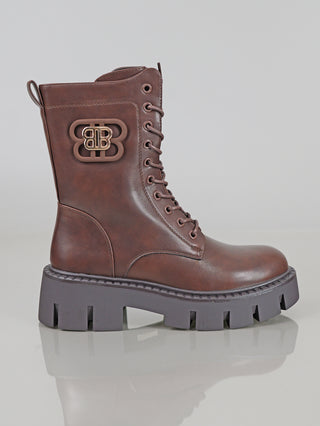Der OFF#DLY Boot BB brown zeigt einen braunen Schnürstiefel aus Polyurethan mit dicker, schwarzer Gummisohle, seitlichem Reißverschluss, dekorativem Metalllogo am Schaft und tonalem Zuglaschen-Detail.