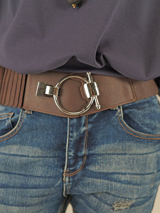 Nahaufnahme eines braunen OFF#DLY Gürtel Ringschliesse mit großer silberner Schnalle, getragen über blauen Jeans. Der Gürtel ist elastisch und aus Polyurethan, stilvoll kombiniert mit einem locker eingesteckten dunklen Oberteil.
