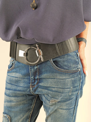 Nahaufnahme eines dunkelblauen, leicht zerstörten Jeans-Looks mit dem OFF#DLY Gürtel Ringschliesse black, einem elastischen, breiten schwarzen Gürtel mit markanter silberner O-Ring-Schnalle, getragen über einem dunklen, eingesteckten Oberteil.