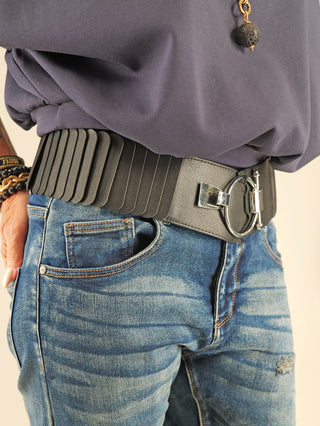 Nahaufnahme eines Taillenbereichs mit dem OFF#DLY Gürtel Ringschliesse black, einem elastischen, schwarzen Gürtel mit silberfarbener, runder Schnalle und überlappenden rechteckigen Laschen, getragen über blauen Jeans.