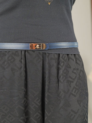 Eine Person trägt den OFF#DLY Gürtel Leder blue, einen schmalen blauen Ledergürtel mit goldener Drehverschluss-Schnalle, der eine schwarze, mit Buchstaben verzierte, eingesteckte Rock-Taille betont.