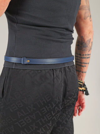 Person von hinten mit floralem Tattoo und Schmuck trägt den OFF#DLY Gürtel Leder blue, einen schmalen, strukturierten blauen Ledergürtel mit goldfarbener Schließe, kombiniert mit schwarzem Tanktop und bedruckter Hose.