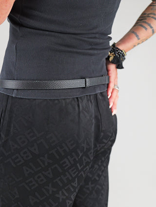 Seitlicher Blick auf den OFF#DLY Gürtel Leder black, einen schmalen, schwarzen Ledergürtel mit goldfarbener Schnalle, getragen über schwarzen ALIX THE LABEL Hosen.