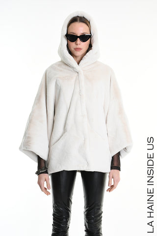 Eine Frau trägt die La Haine Jacket white, eine gefütterte Kunstfell-Sportjacke mit Kapuze. Dazu kombiniert sie enge schwarze Lederleggings und schwarze, schmale Cat-Eye-Sonnenbrillen.