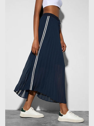BSB Skirt French Navy: Fließender Plissee-Rock in Navy mit weißen Seitenstreifen, kombiniert mit weißen Sneakern mit dunkelgrünem Fersenbereich und einem weißen Crop-Top, ideal für sportlich-elegante Outfits.