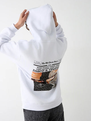 Person zieht die Kapuze des weißen BSB Bluse 210084 Hoodies hoch, mit Zeitungsdruck NEW STUDY FINDS THAT THE LADIES JUST WANT DISCO & TEQUILA und Bild einer Frau in Glitzerkleidung.
