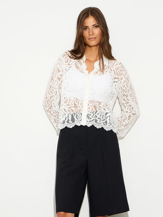 BSB Shirt 216021 offwhite: Modell trägt transparente, langärmelige Spitzenbluse mit floralem Muster und Knopfleiste, kombiniert mit hoch taillierten, schwarzen Shorts, vor weißem Hintergrund.