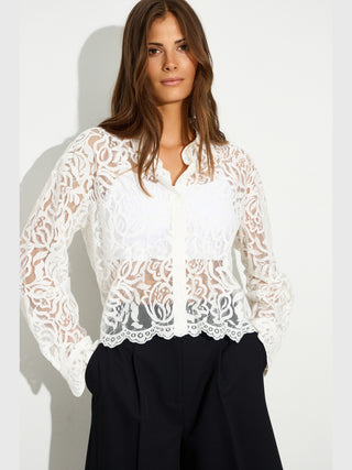 Junge Frau trägt BSB Shirt 216021 offwhite, eine transparente Spitzenbluse mit floralem Muster und Knopfleiste, über einem weißen Top, kombiniert mit schwarzen, weit geschnittenen Hosen.
