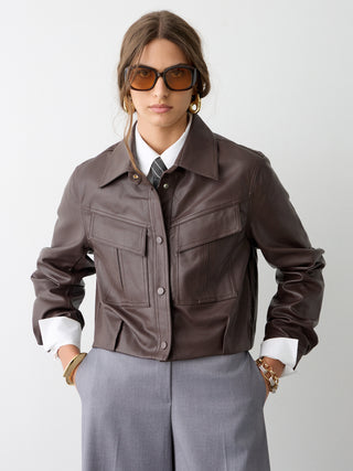 BSB Jacke 217002 brown: Junge Person trägt eine kastige, braune Kunstlederjacke mit Brusttaschen und Druckknöpfen, kombiniert mit weißem Hemd, Krawatte und grau melierten Hosen für einen modernen, eleganten Look.