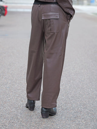 Die BSB Hose 212003 chocolate zeigt eine lässige, weite Kunstlederhose mit elastischem Bund und seitlichen Eingrifftaschen, kombiniert mit schwarzen Lederstiefeletten auf einem Gehweg.