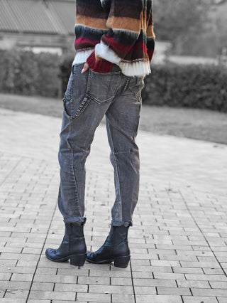 Person trägt OFF#DLY Denim Beatrice black washed, lässige graue Jeans mit markanter Waschung und auffälligen Taschen. Kombiniert mit schwarzen Lederstiefeln und gestreiftem Pullover.