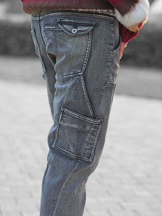 Eine Person trägt OFF#DLY Denim Beatrice black washed Jeans mit markanten Taschen und lässigem Destroyed-Style, stehend auf einer gepflasterten Fläche. Ein roter und weißer Pullover ist teilweise sichtbar.