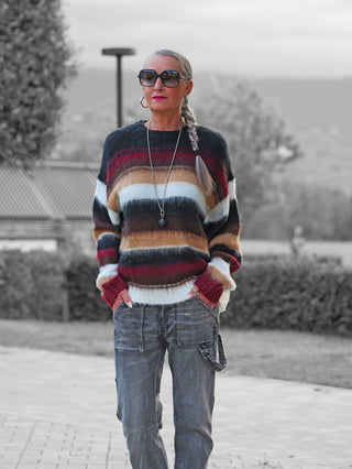 Die Frau trägt den OFF#DLY Pulli Silvana Stripe black/bordeaux, ein weiches Statement-Stück mit breiten Streifen, kombiniert mit grauen Cargo-Jeans, perfektioniert durch Sonnenbrille und Schmuck.