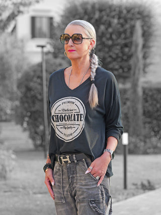 Frau trägt das OFF#DLY Longsleeve Chocolate black mit rundem Logo-Aufdruck auf tiefem Anthrazit-T-Shirt. Kombiniert mit Cargo-Hose, Gürtel und Schmuck, wirkt ihr Look lässig und modern.