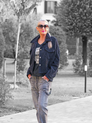 Die OFF#DLY Jacke Zaira black wird von einer Frau im Park getragen, zeigt kurze Form und sportliche aufgesetzte Brusttaschen, ideal für einen lässigen Look über einem Printshirt.