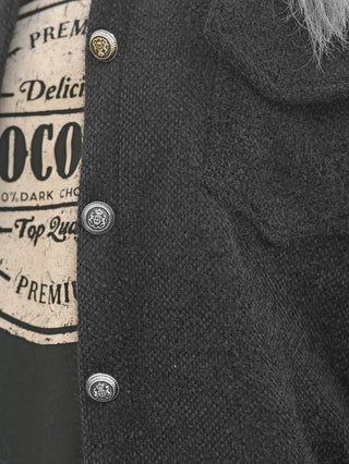 Nahaufnahme der OFF#DLY Jacke Zaira black, ein grob gestricktes schwarzes Oberteil mit dekorativen Metallknöpfen, die ein Krone-Wappen-Motiv zeigen, getragen über einem COCO/100% Dark Chocolate Printshirt.