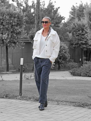 Eine Frau trägt die OFF#DLY Jacke Zaira offwhite, die durch ihren kurzen Schnitt und markante Knöpfe besticht. Die Jacke wirkt modern und bietet sportlichen Komfort.