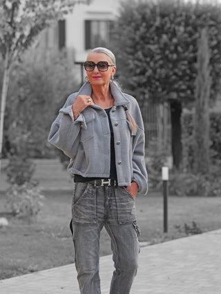 Ältere Frau trägt die OFF#DLY Jacke Zaira grey, einen kurz geschnittenen, stilvollen Allrounder mit Hemdkragen und aufgesetzten Taschen, kombiniert mit schwarzem Top und grauen Cargo-Hosen.