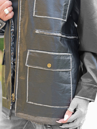 Nahaufnahme des OFF#DLY Fake Leather Blazer Tatiana black mit großer Pattentasche, kontrastierenden Nähten, sichtbarem Reißverschluss, subtiler Lederoptik und der Hand mit weißen, spitzen Nägeln und Silberringen.