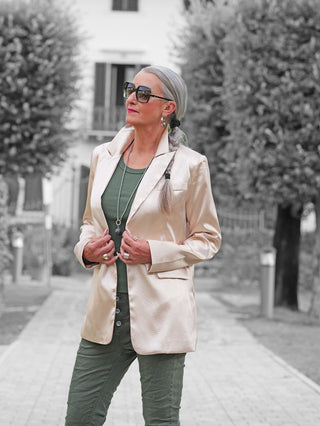 Die reife Frau trägt den OFF#DLY Blazer Rosalia champagner mit Reverskragen, strukturiertem Kunstleder-Look und Pattentaschen, kombiniert mit einem olivgrünen Outfit und stilvollen Accessoires.