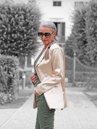 Frau in OFF#DLY Blazer Rosalia champagner mit Reverskragen und Pattentaschen, lässig getragen über einem dunkelgrünen Oberteil, präsentiert klassische Eleganz und modernen Stil in einem strukturierten Kunstleder-Look.