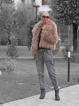 Frau trägt OFF#DLY Fake Fur Jacke beige, flauschig und voluminös, über dunklem Oberteil. Kombiniert mit grauen Cargo-Jeans, schwarzem Gürtel und spitzen schwarzen Stiefeletten für modischen Streetstyle-Look.