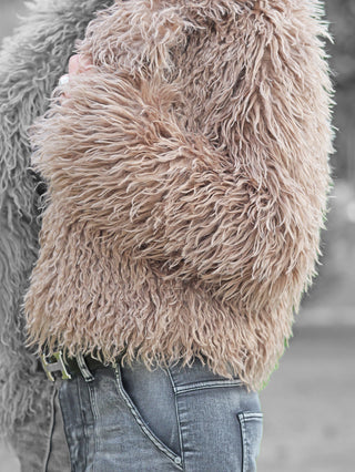 Nahaufnahme der OFF#DLY Fake Fur Jacke beige, die eine flauschige, weiche Textur zeigt, kombiniert mit ausgewaschenen Jeans und Gürtel. Ein Ring an der Hand ergänzt den stilvollen Winterlook.