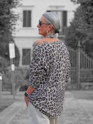 Frau mit grauem Zopf trägt das OFF#DLY Longsleeve Astrid beige/black im Leo-Print, kombiniert mit hellen Hosen, während sie lässig in einer ruhigen Straße steht.
