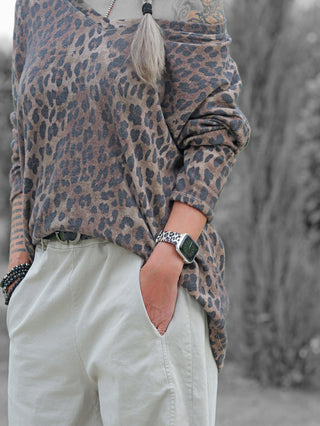 Person trägt das OFF#DLY Longsleeve Astrid camel/black im Leo-Print, locker in beige Hose gesteckt. Smartwatch mit passendem Band und beaded Armbänder ergänzen den Look.